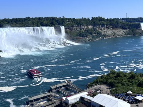 A stunning aerial shot of Niagara Falls with a tour boat in the foreground under a clear blue sky.