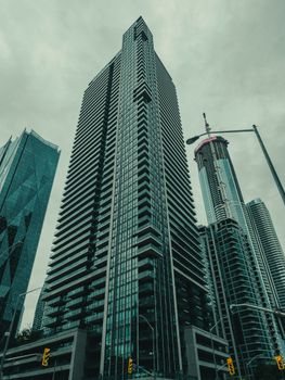 A towering modern skyscraper amidst an urban skyline under cloudy skies, capturing city life.