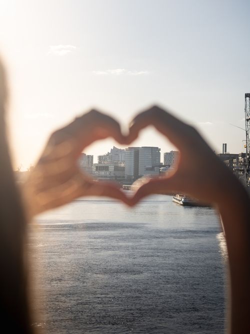Free Silhouette of hands forming a heart shape framing Hamburg's skyline at sunset. Stock Photo