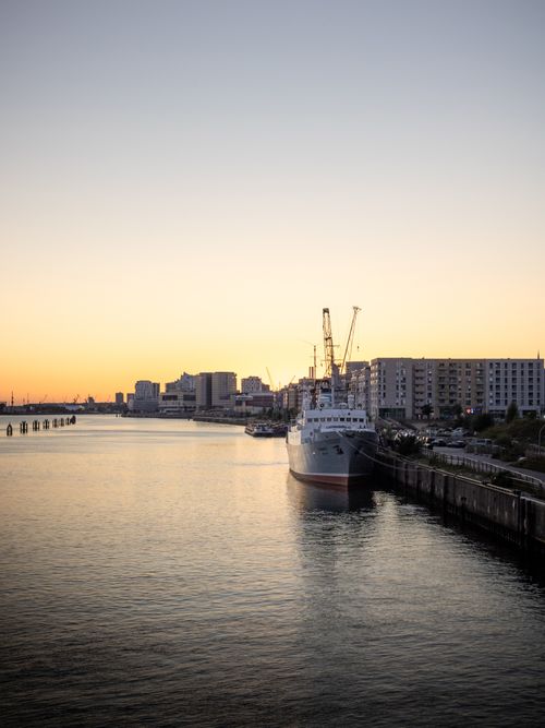 Free Tranquil sunset over Hamburg harbor featuring a docked ship and city skyline, capturing a peaceful urban evening. Stock Photo