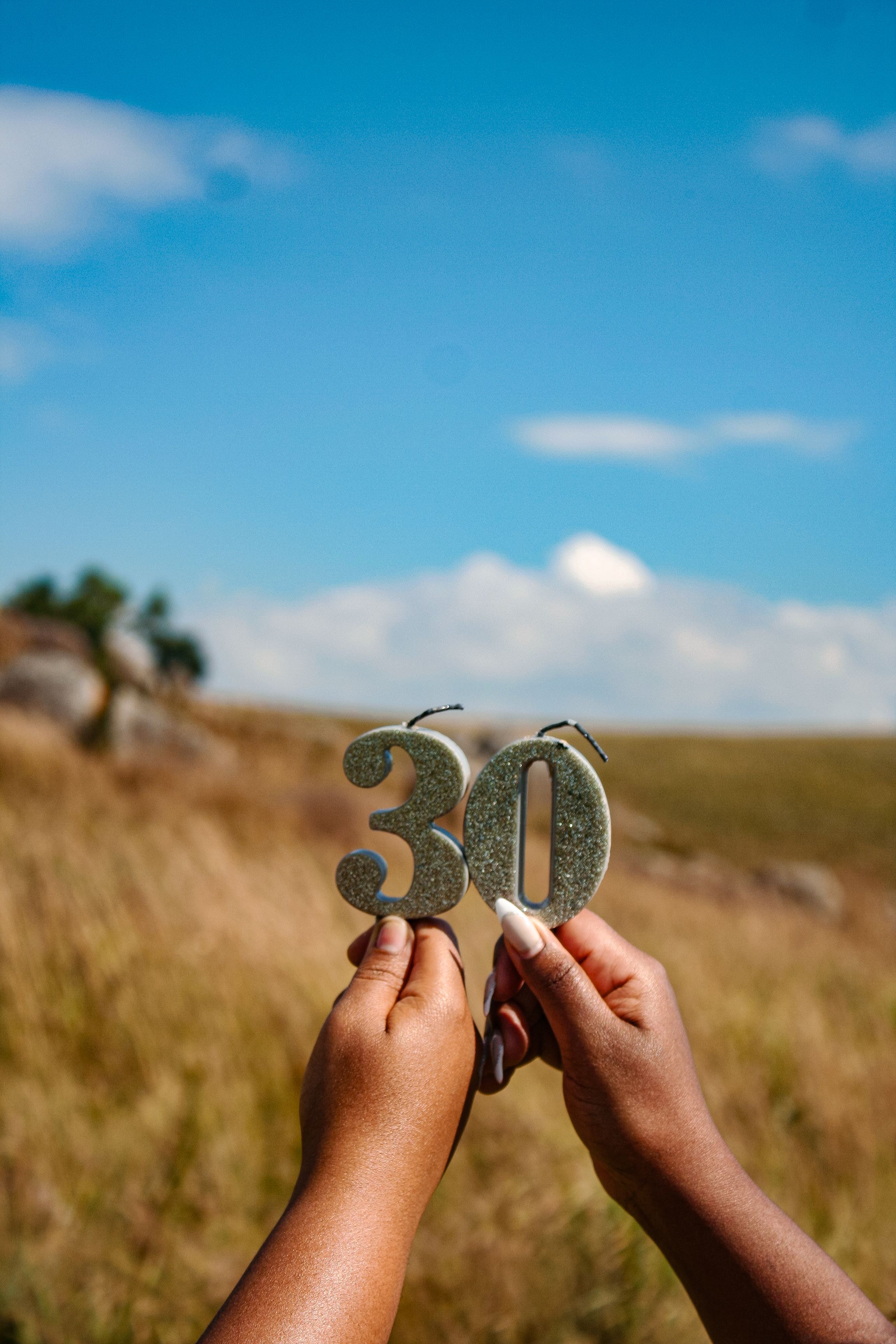 Hands holding a glittering '30' sign in a scenic outdoor setting in Eswatini.