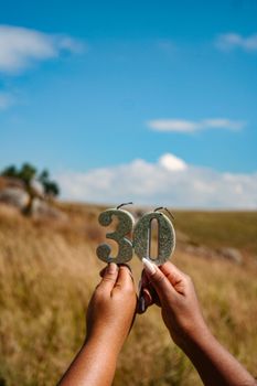 Hands holding a glittering '30' sign in a scenic outdoor setting in Eswatini.