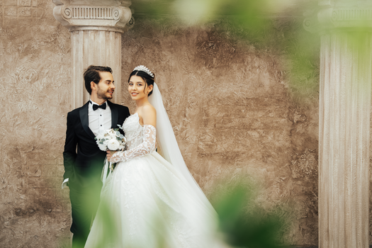 A classic wedding portrait of a couple in elegant attire, set against historic columns in Antalya, Türkiye.