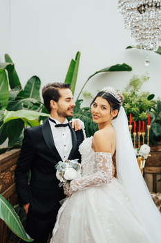 A stylish wedding couple poses in an elegant indoor setting with lush greenery.
