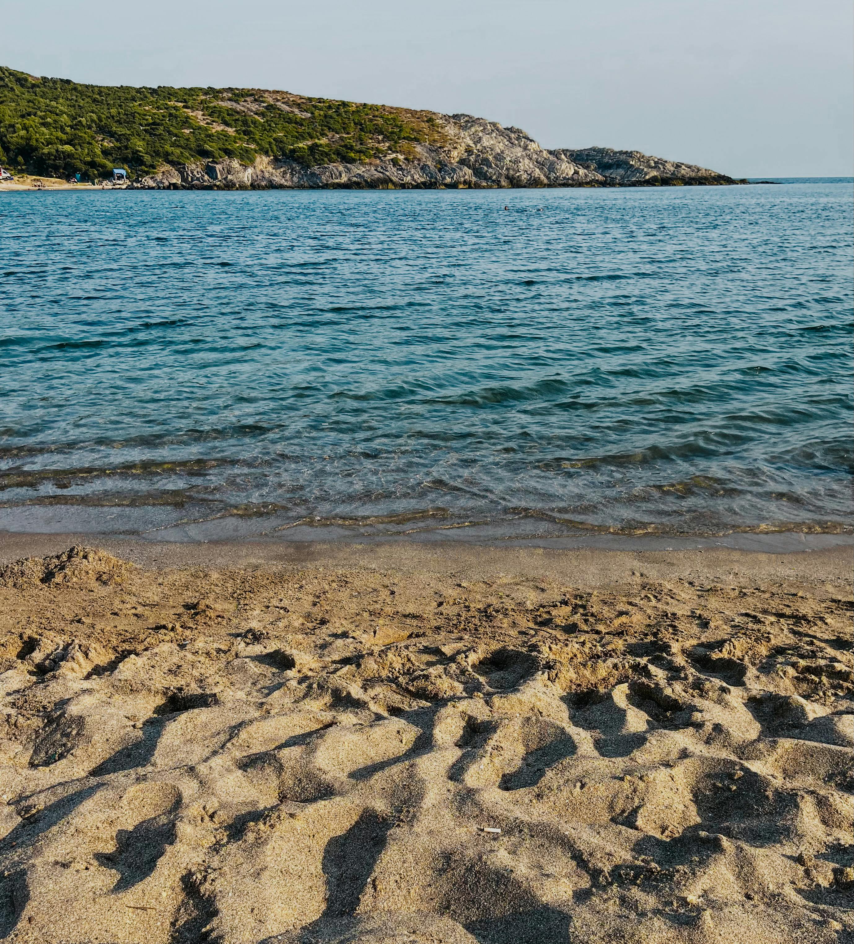 在宁静的海滩上，清澈的海浪拍打着岸边，明亮的天空映照着远处山丘的轮廓
