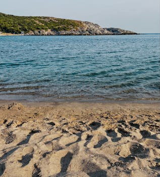 在宁静的海滩上，清澈的海浪拍打着岸边，明亮的天空映照着远处山丘的轮廓