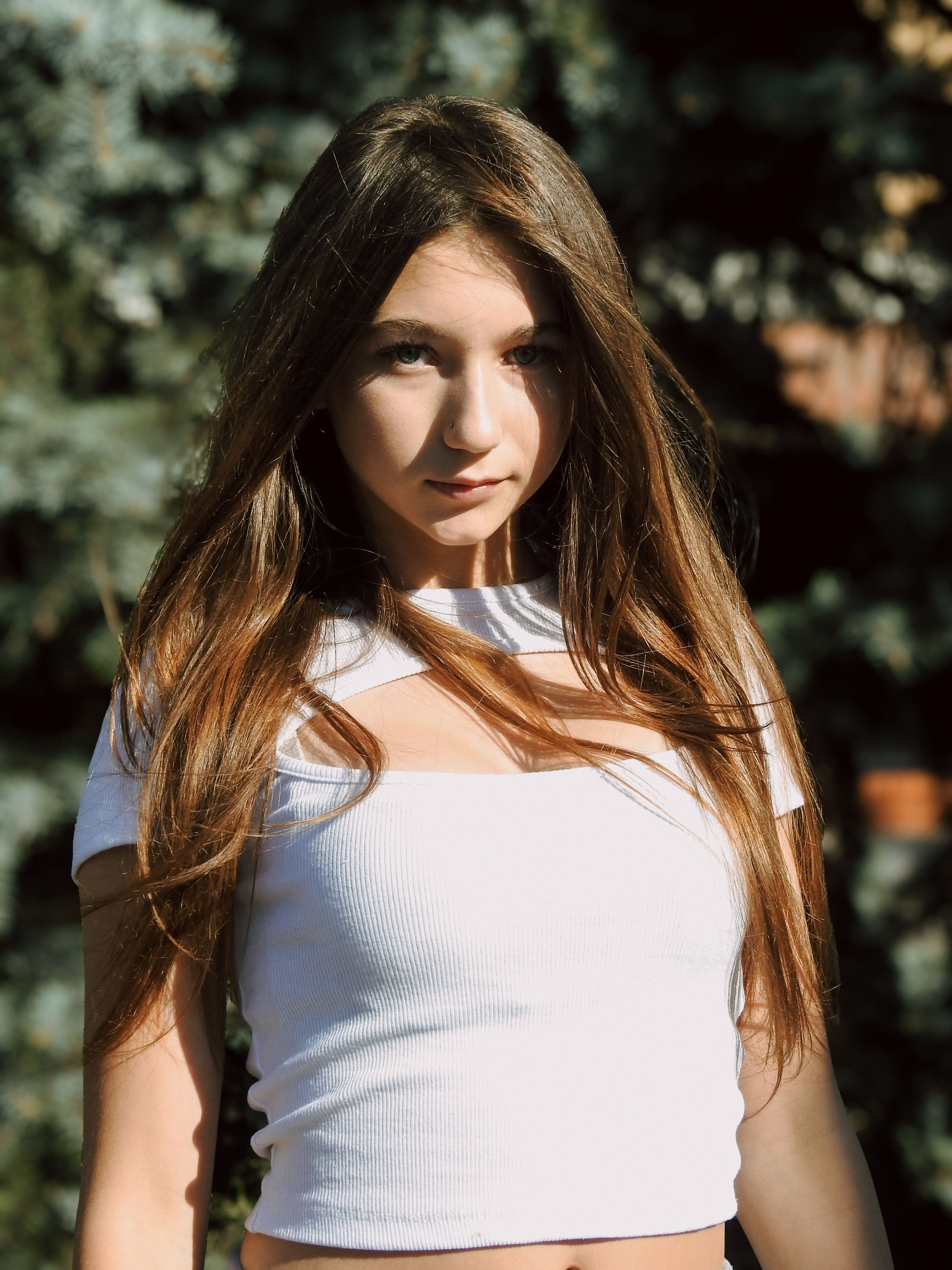 A young woman poses outdoors in sunlight, exuding confidence and style.