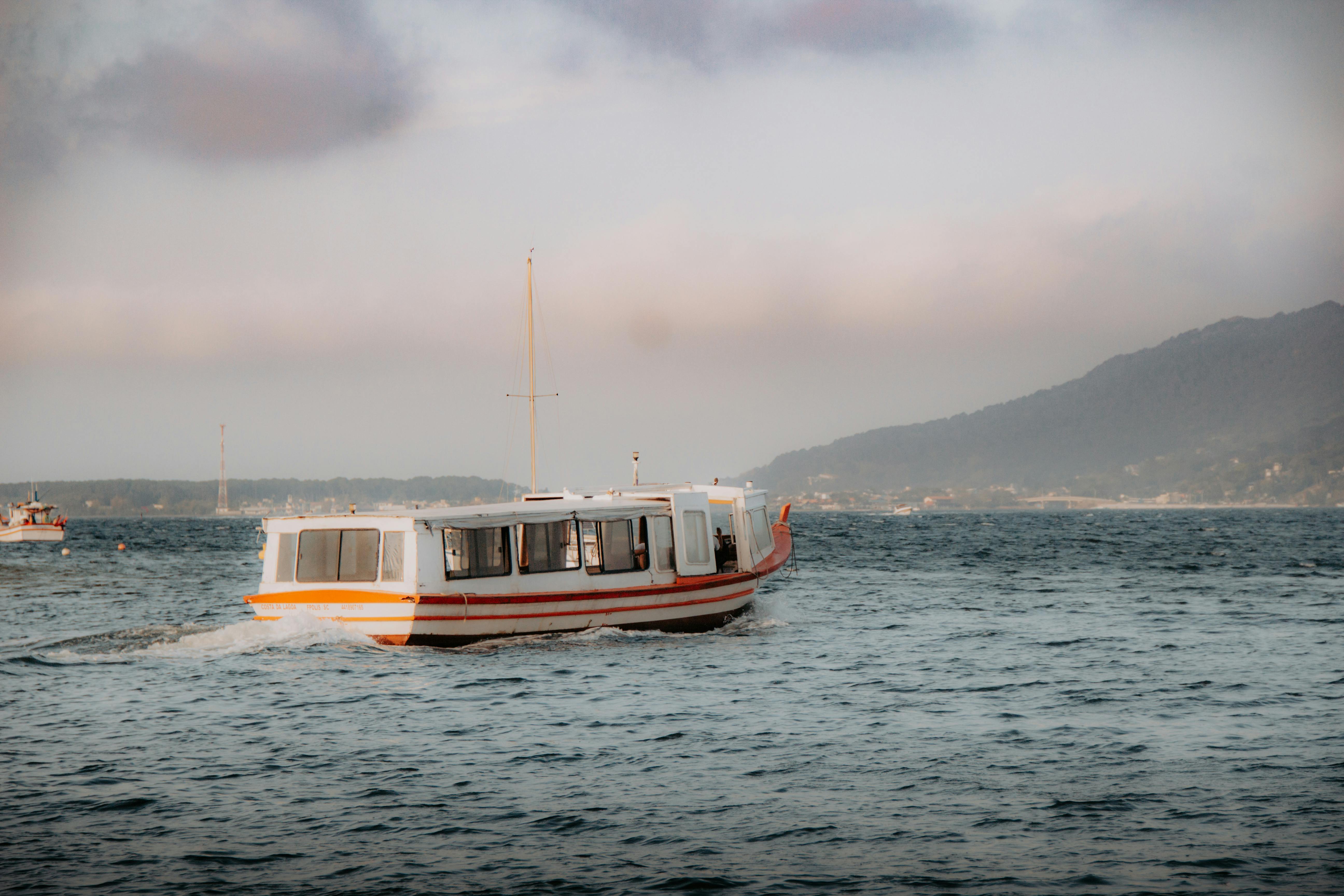 日落时，白色的船在平静的水域中航行，而背后是山脉