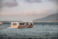 日落时，白色的船在平静的水域中航行，而背后是山脉