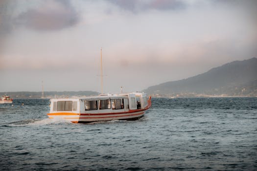 日落时，白色的船在平静的水域中航行，而背后是山脉