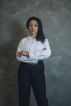 Confident woman in formal wear against a neutral background, arms crossed