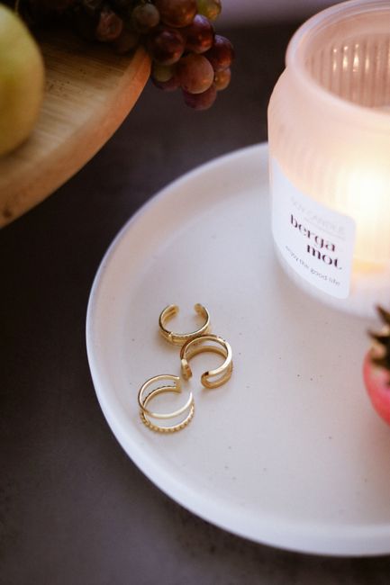 Three gold rings elegantly displayed on a white tray beside a lit candle. Cozy ambiance.