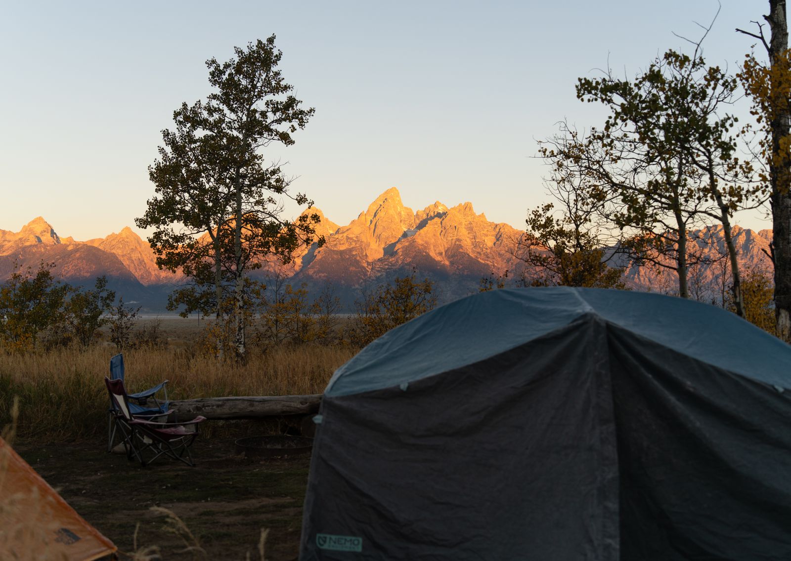 Tent pitched in a meadow as golden-hour light hits the mountain peaks behind