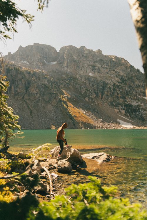 Free Hiker on rocky lake shore with mountainous backdrop in Wyoming's wilderness. Stock Photo