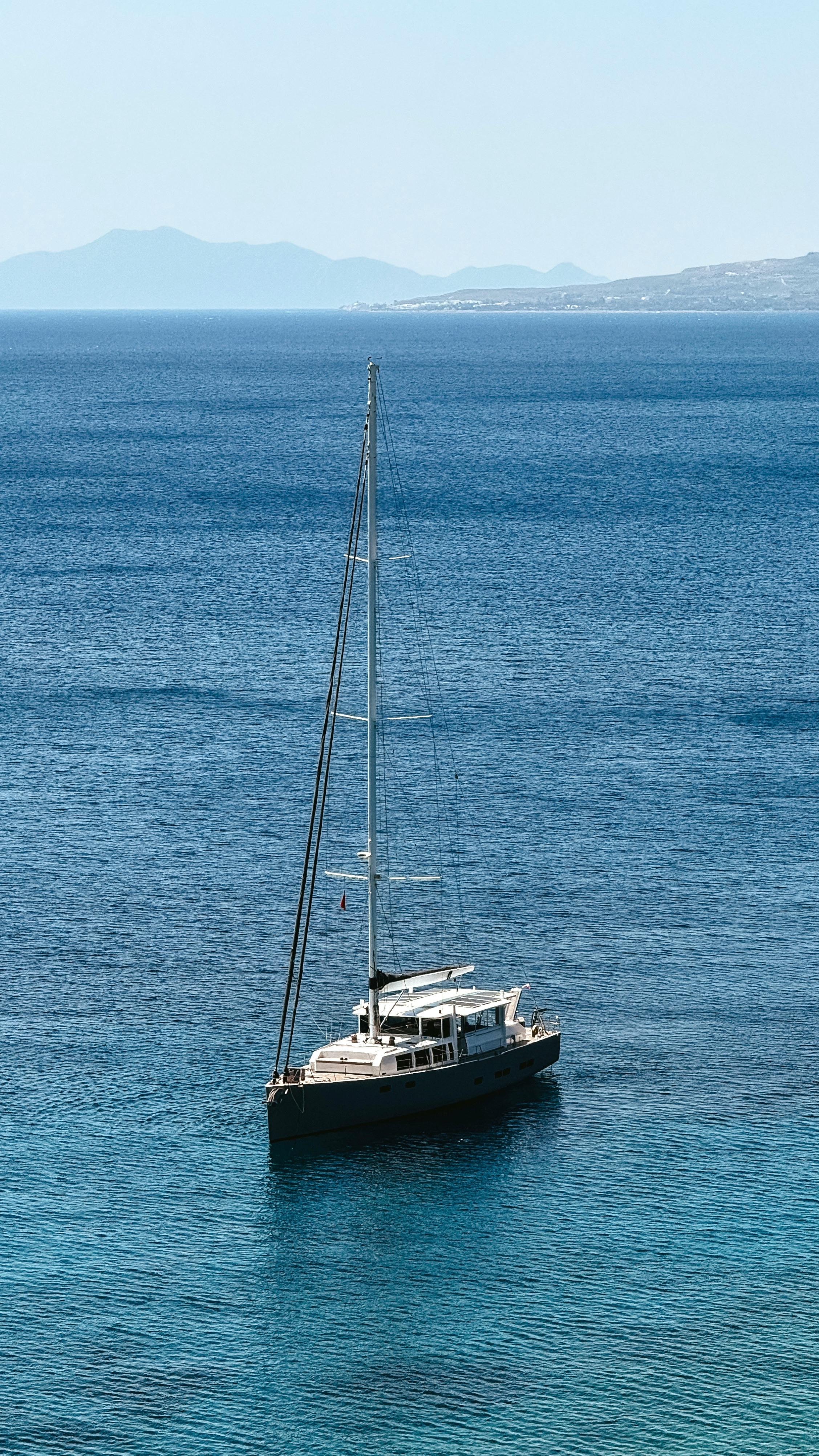 一艘孤独的帆船漂浮在明亮的夏日天空下，平静的蓝色海洋上