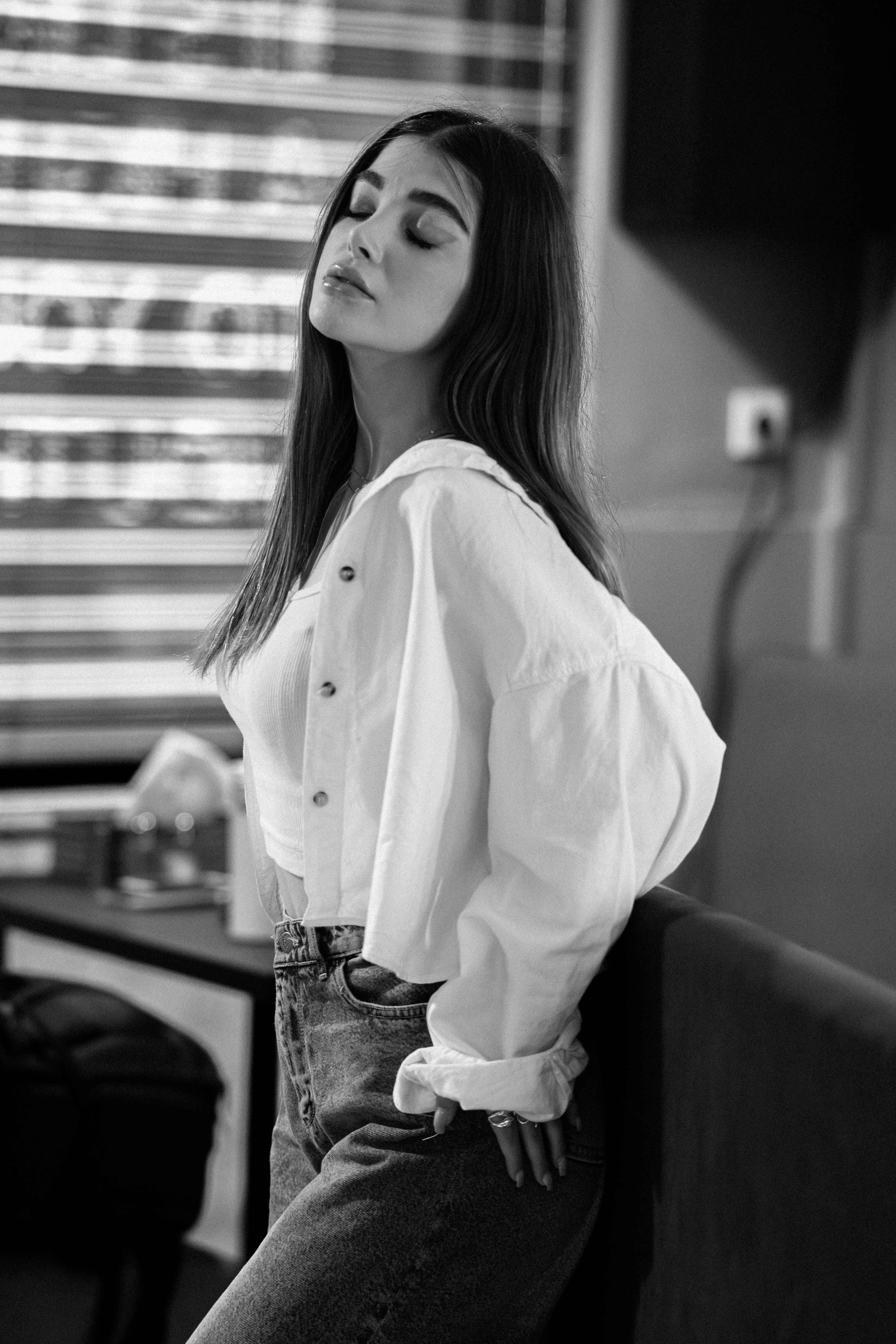 Black and white portrait of a stylish young woman in a relaxed pose indoors.