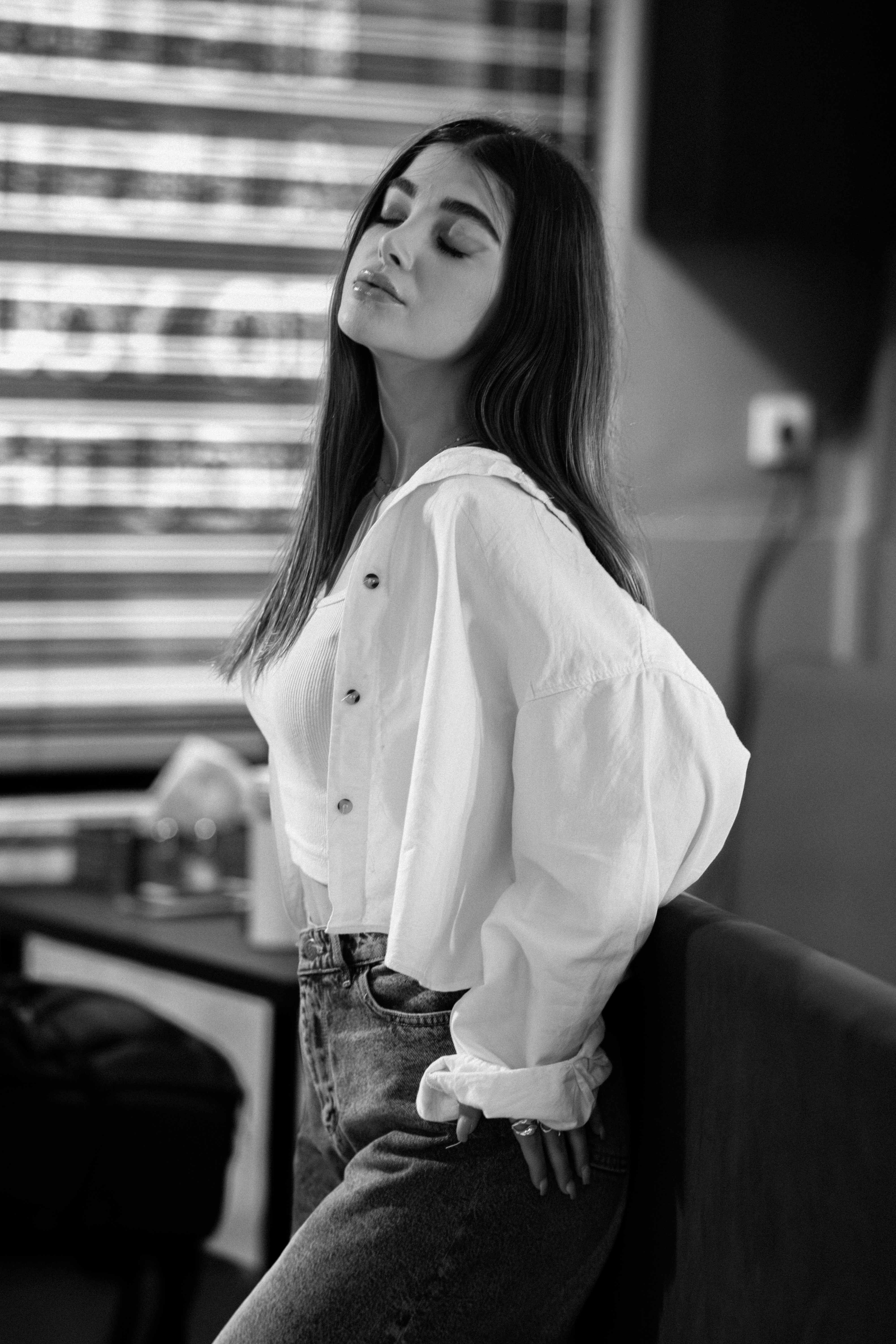 Stylish monochrome portrait of a young woman in a white shirt, showcasing elegance and confidence indoors.