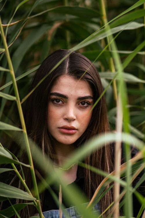 Free A striking portrait of a woman surrounded by green reeds, showcasing natural beauty and serenity. Stock Photo