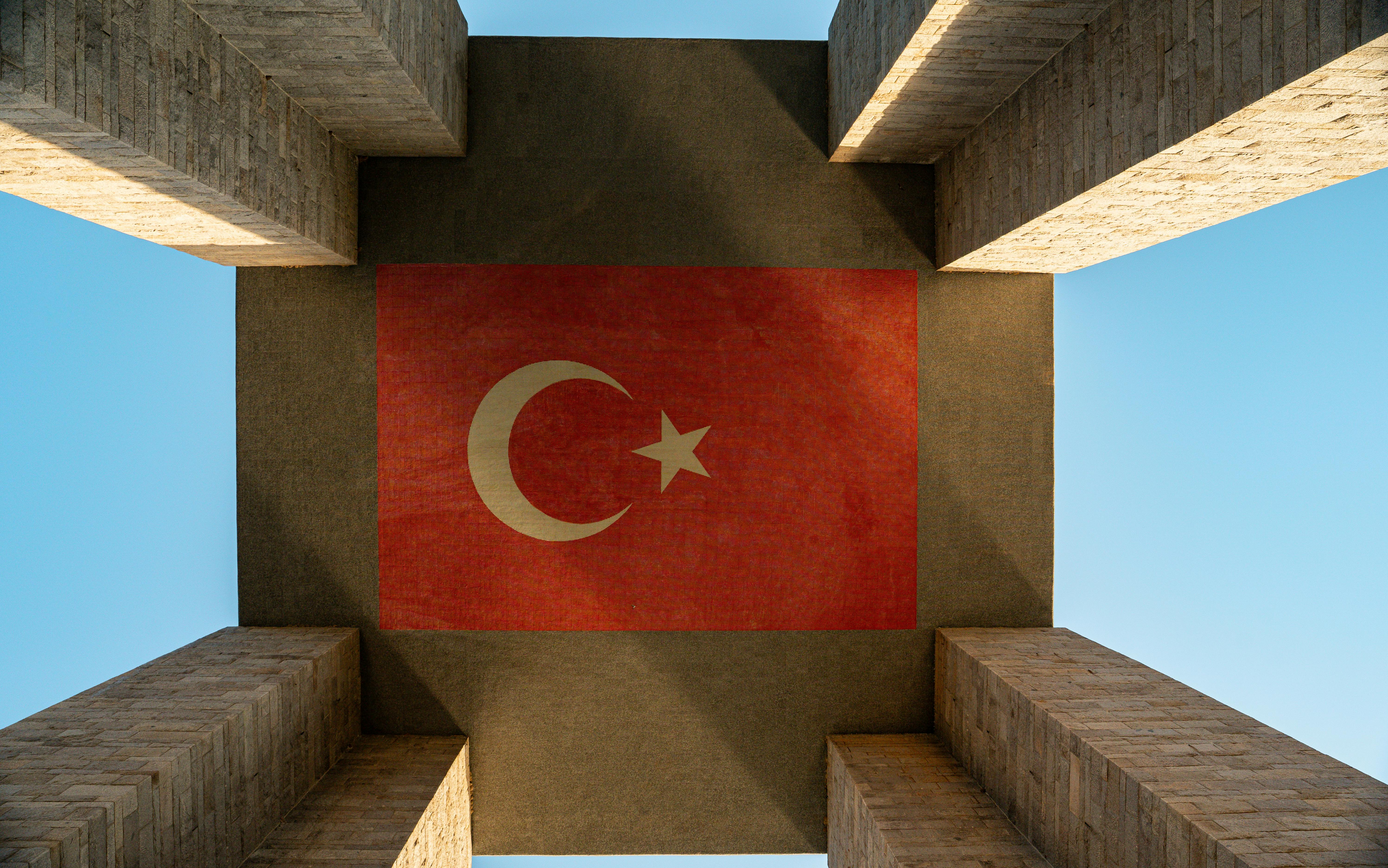 在晴朗的天空下，一个巨大的建筑的下面，可以看到一面向上的土耳其国旗