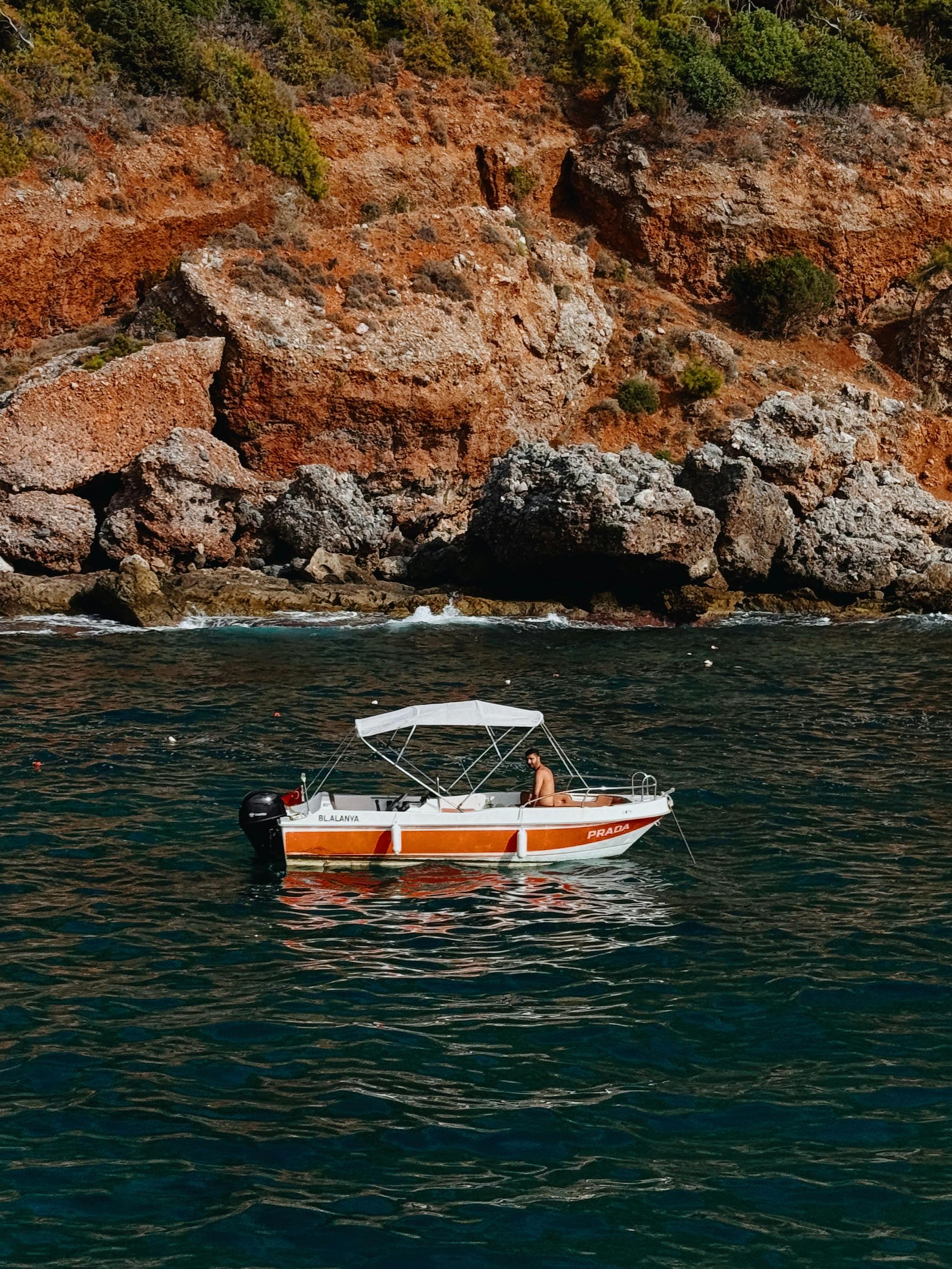 一艘小船在晴朗的天空下航行，土耳其的风景优美的岩石海岸线上