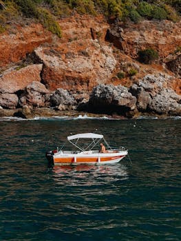 一艘小船在晴朗的天空下航行，土耳其的风景优美的岩石海岸线上