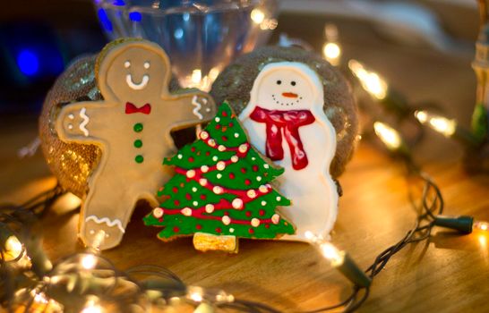 Gingerbread man, snowman, and Christmas tree cookies surrounded by holiday lights on a warm background.