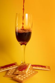 Artistic capture of wine pouring into a glass, placed on crackers against a vivid yellow background.