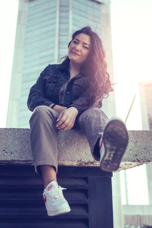 Free Young woman sitting on a ledge in an urban setting, showcasing a casual fashion style. Stock Photo
