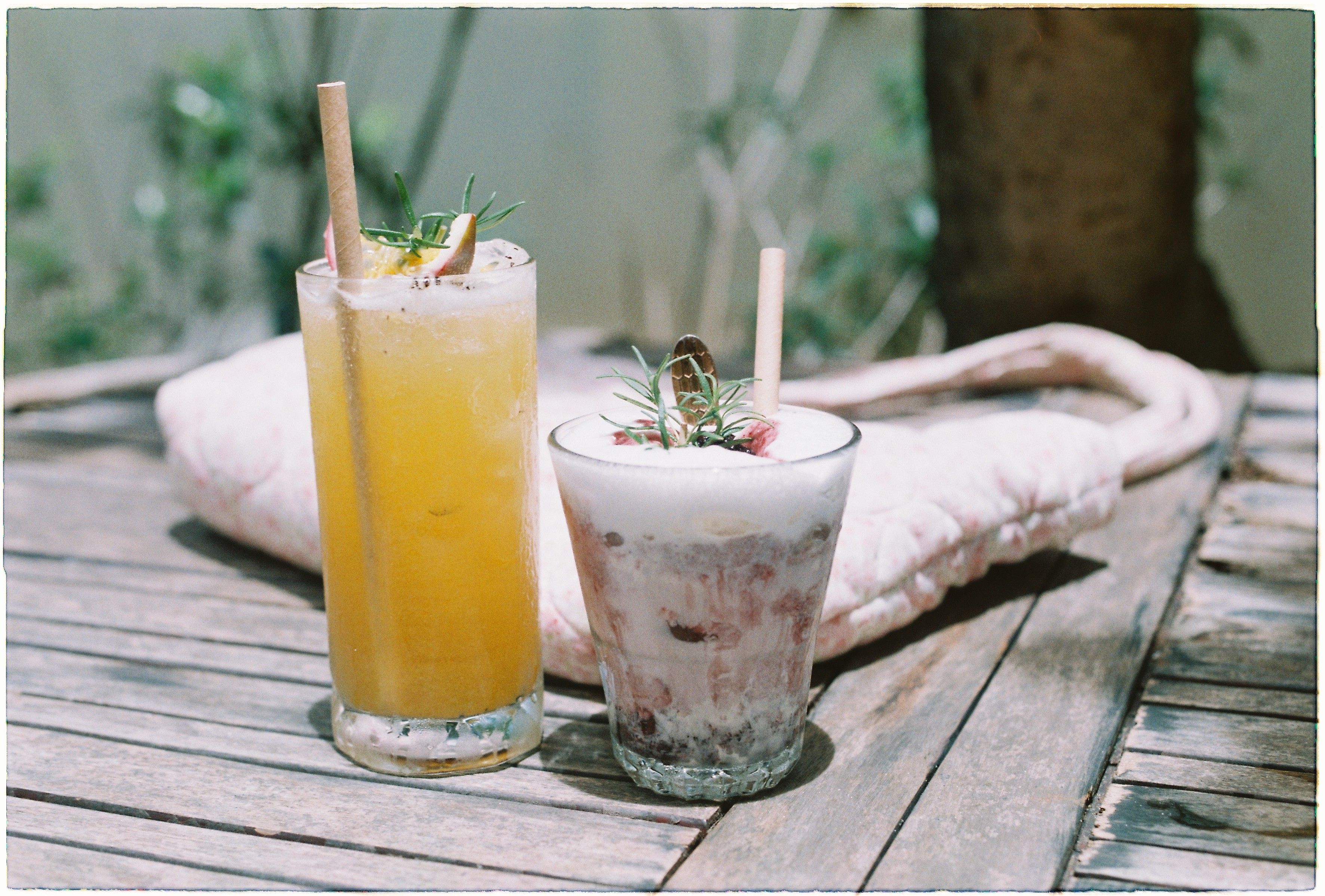Two refreshing summer drinks on a rustic wooden table outdoors, perfect for a sunny day.