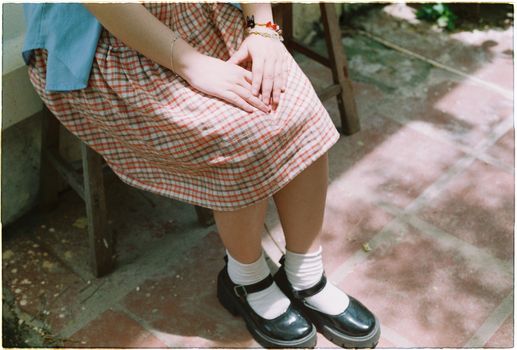 A young girl wearing white socks and black shoes sits outside on a sunny day.