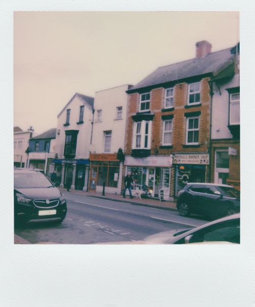 Free Polaroid photo capturing a quaint street with classic buildings and parked cars. Stock Photo