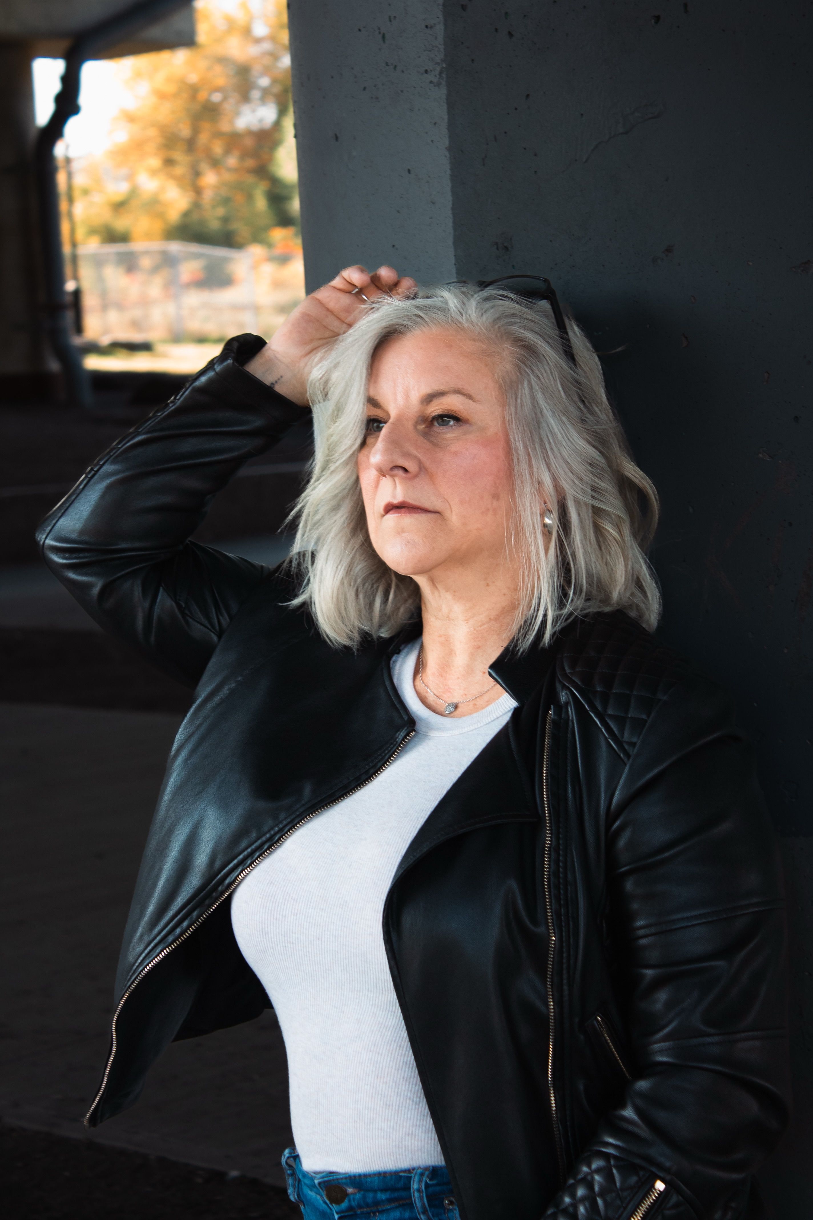 Stylish mature woman in leather jacket posing outdoors with natural light.