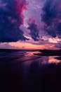 一个生动的紫色日落和一个戏剧性的云彩出现在一个宁静的海滩上，这迷人的景色让人着迷