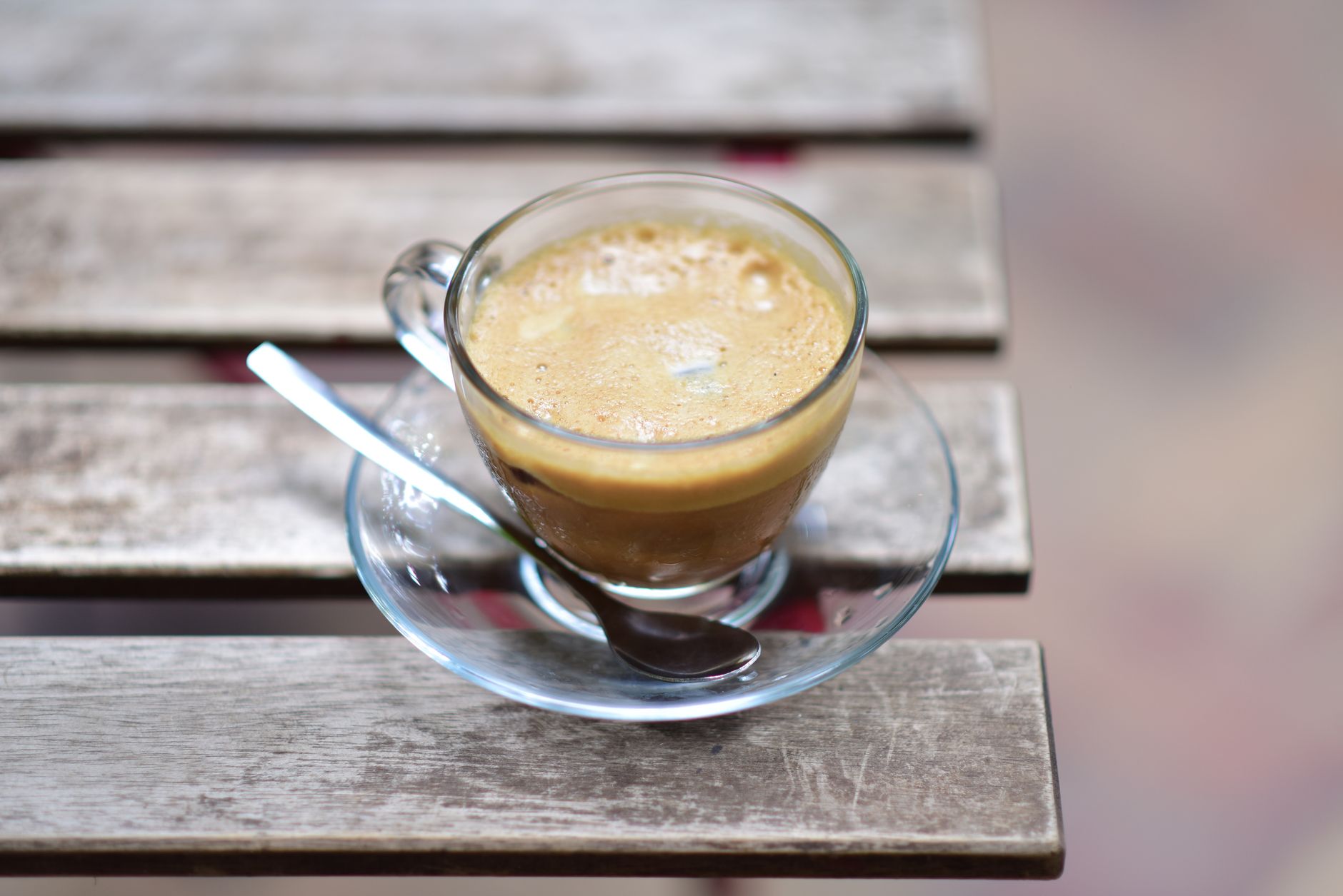 A glass cup of espresso coffee on a rustic wooden table with a spoon.