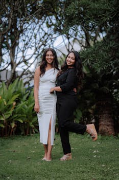 Two women posing together in a garden, showcasing smiles and stylish outfits.