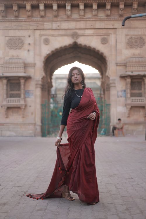 Free Elegant woman in red saree posing in front of historical archway, showcasing traditional fashion. Stock Photo