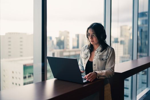 A woman using a laptop by a large window in a bright, modern office setting.
