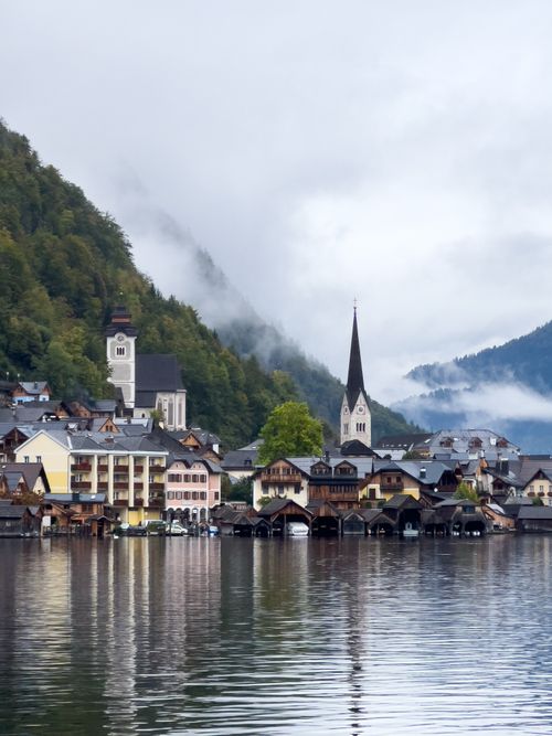 Free Mist covers a picturesque village by the lake surrounded by hills, featuring a notable church steeple. Stock Photo
