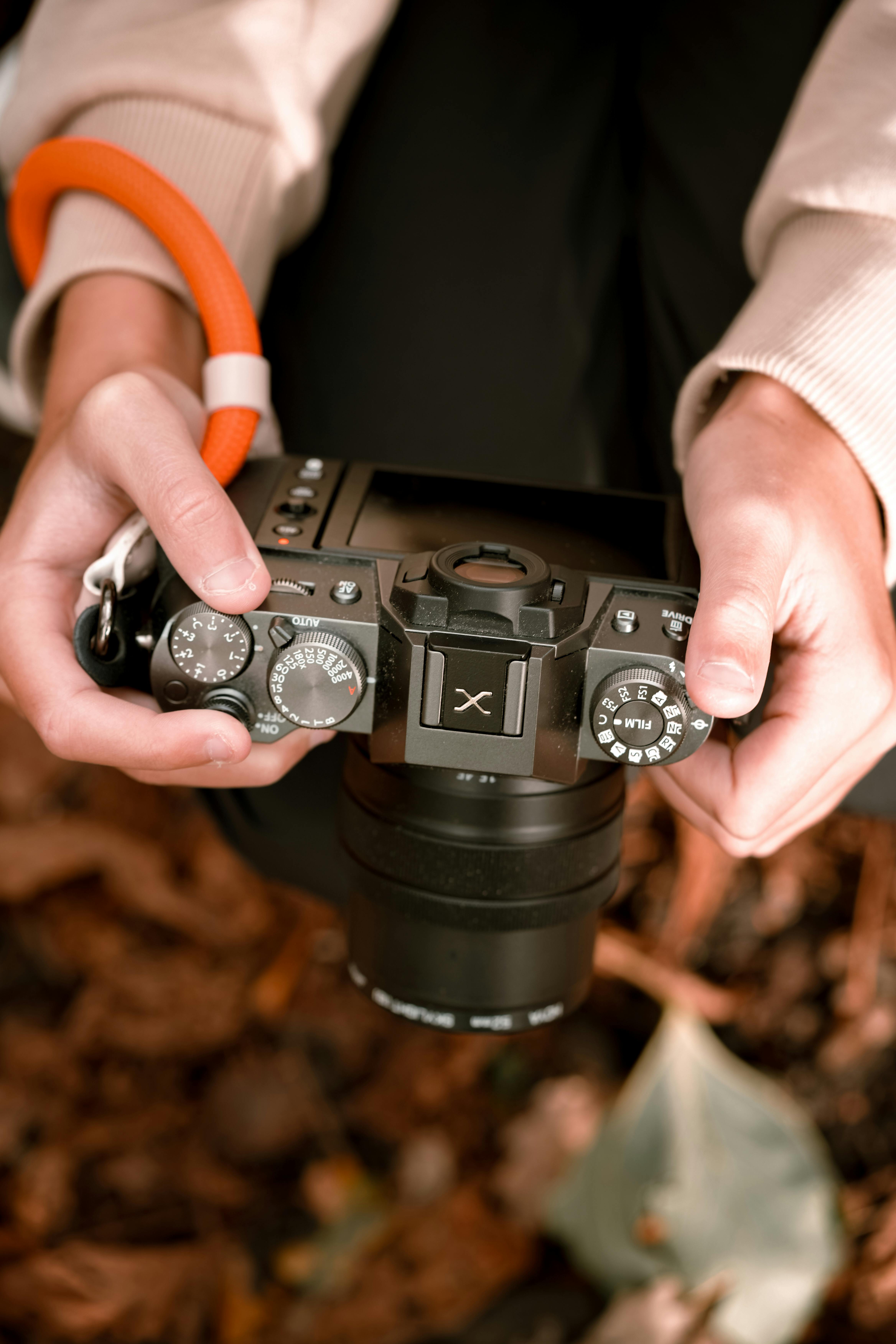 Free Close-up of hands holding a camera with autumn leaves in the background. Stock Photo
