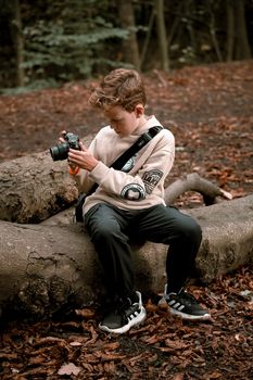 Boy sitting on a log in autumn forest, exploring photography with a camera.