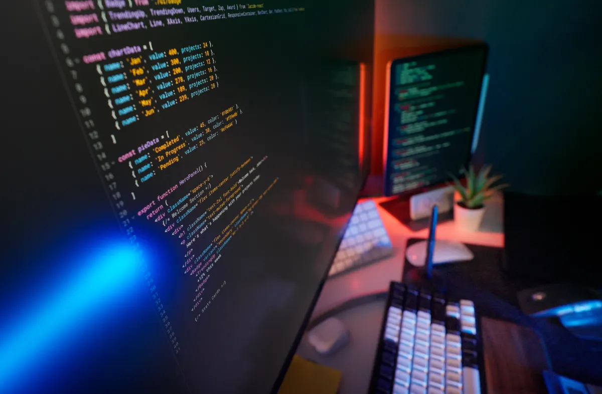 A workstation lit in red and blue with colour-highlighted code on two monitors, the kind of setup used to connect a trading strategy to the IBKR API