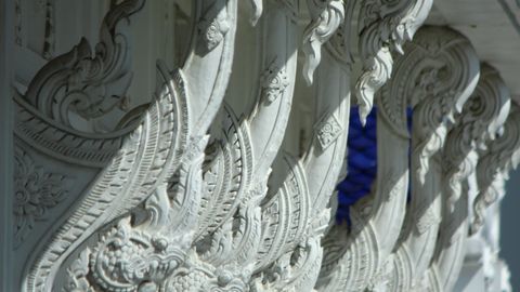 Ornate white carvings decorate a temple roof, showcasing intricate traditional design.