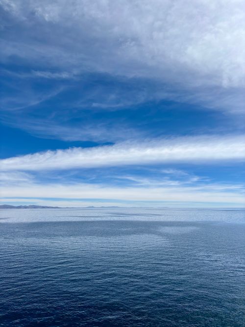 Free A serene view of Lake Titicaca with a vast blue sky and wispy clouds, capturing natural beauty and calmness. Stock Photo