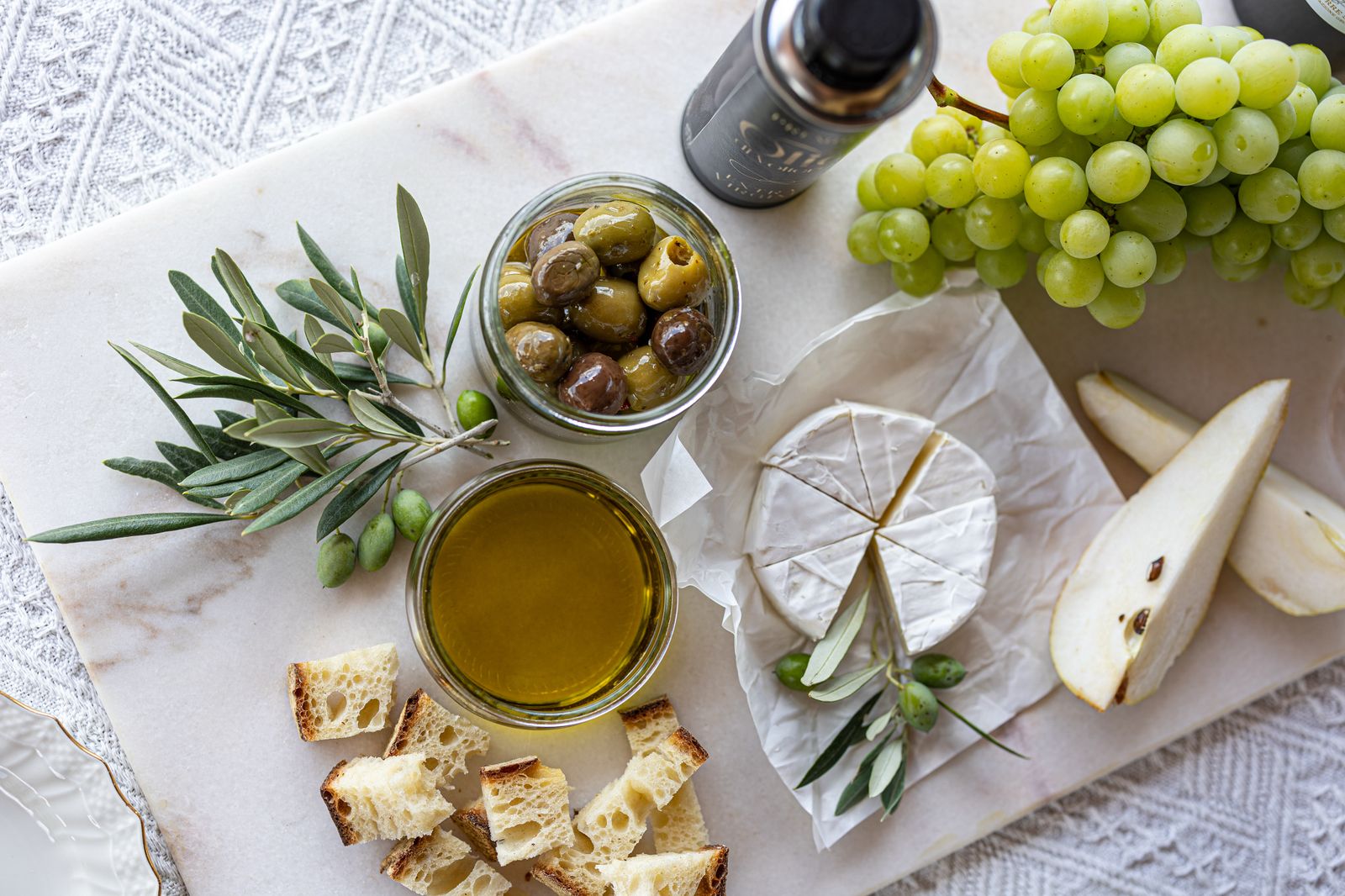 Marble board with soft rind cheese, green grapes, pear slices, olives, olive oil and bread cubes