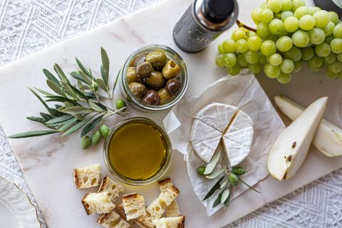 Marble board with soft rind cheese, green grapes, pear slices, olives, olive oil and bread cubes