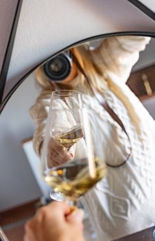 Artistic reflection shot capturing a person holding a glass of white wine through a mirror.