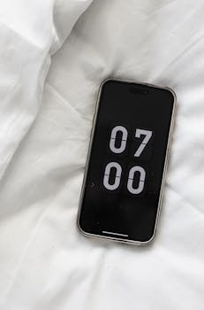 A smartphone displaying 7:00 AM with a minimalist design on a white bed setting.