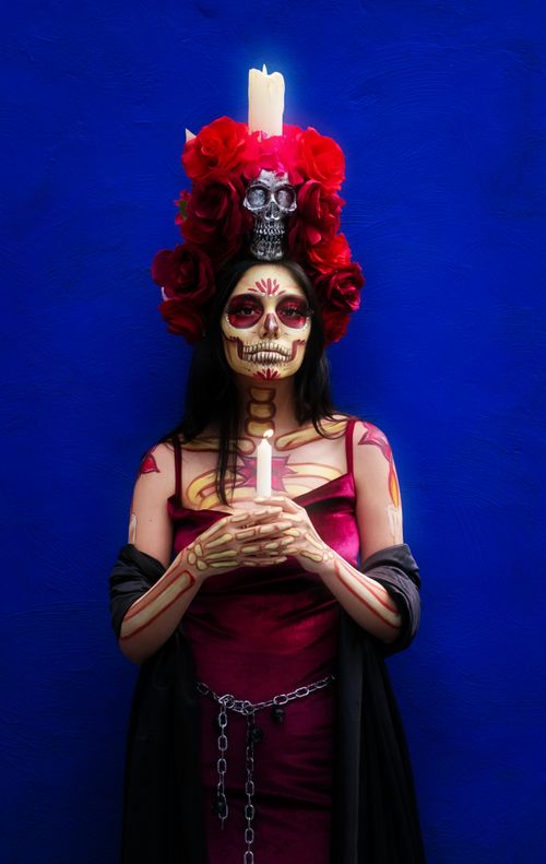 Free A woman dressed as a Catrina for Day of the Dead, holding a candle, with artistic makeup and a skull headdress. Stock Photo