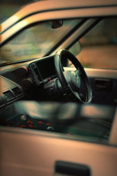Close-up view of a vintage car interior showing the steering wheel with a blurred window inside.