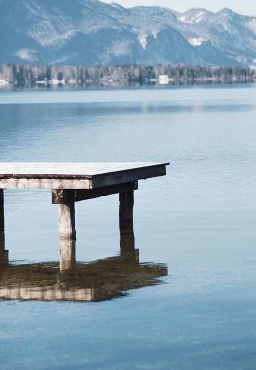 Free Serene landscape of a snowy pier and Austrian Alps reflected in a calm lake under a bright winter sky. Stock Photo